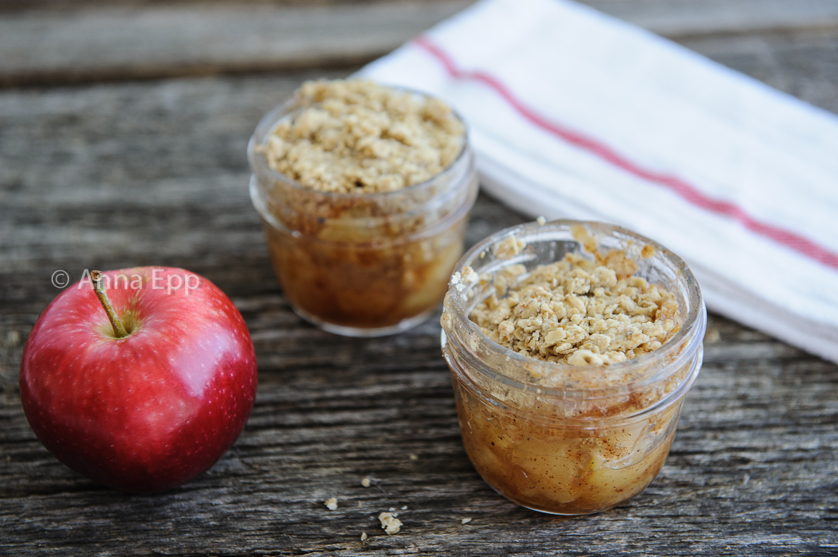 two mason jar apple crisps with a red apple and a white napkin with red ribbing on it